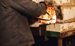 Bearded man blacksmith gets a red-hot billet out of the furnace