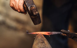 Blacksmith makes an artistic forging of hot metal on the anvil.