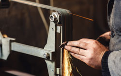 Close-up master grinds the knife on a belt grinder and many sparks are produced