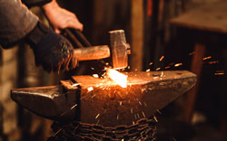 The blacksmith manually forging the red-hot metal on the anvil in smithy with spark fireworks